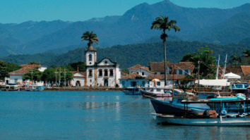 Vista de Paraty, no litoral do Rio de Janeiro, com igrejas históricas, casas coloniais e barcos coloridos ancorados no cais, tendo a serra ao fundo