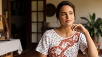 Mulher brasileira usando blusa de crochê artesanal com pontos criativos e gráficos, em ambiente iluminado por luz natural suave.