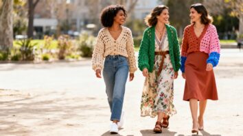 Três mulheres sorrindo ao ar livre, usando cardigãs de crochê modernos e coloridos, representando moda artesanal, amizade e autenticidade feminina.