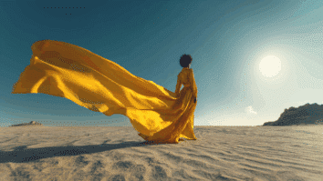 Mulher caminhando em um deserto iluminado pelo sol, vestindo um vestido de seda amarela com uma longa capa esvoaçante, simbolizando liberdade, recomeço e novas possibilidades.