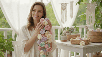 Mulher sorridente segurando flores de crochê coloridas em ambiente iluminado e natural, transmitindo alegria, delicadeza e amor pelo artesanato.