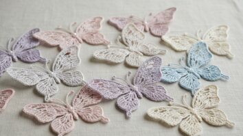 Conjunto de borboletas de crochê artesanais em tons pastel e degradês suaves sobre superfície de linho claro com asas rendadas e detalhes delicados.