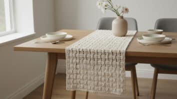 Caminho de mesa em-white com trama moderno-minimalista bem definida, posicionado ao centro de mesa de madeira clara, acompanhado de vaso neutro e flores delicadas.