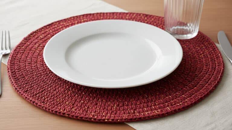 Mesa elegante com sousplat redondo de crochê vinho com detalhes dourados emoldurando prato branco sob luz natural difusa