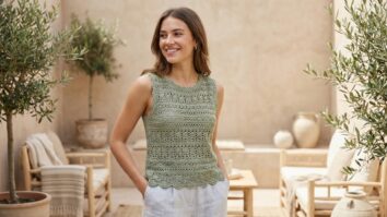 Mulher jovem sorridente usando blusa de crochê artesanal em algodão verde claro com trama delicada e acabamento uniforme, estilo versátil e sustentável para o verão, transmitindo leveza e presença estilosa.