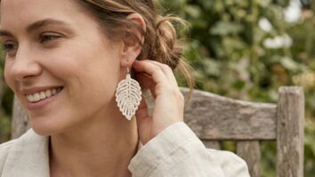 Mulher sorrindo exibindo brincos de crochê em algodão cru, acessórios sustentáveis em ambiente de verão.