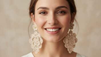 Mulher sorrindo usando brincos de crochê artesanais delicados com ferragens douradas em fundo neutro com iluminação suave