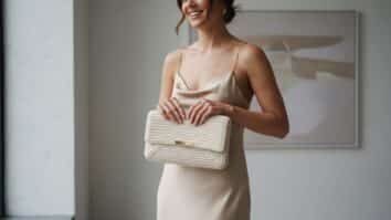 Mulher sorridente segurando uma elegante clutch de crochê em tom marfim com tampa reta e fecho metálico, vestida com roupa minimalista em ambiente com iluminação natural difusa.