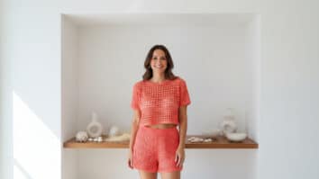 Mulher sorridente em vitrine minimalista usando top curto de crochê coral com textura aberta sob luz natural