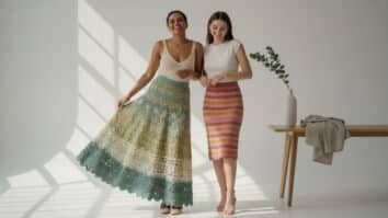 Duas mulheres sorrindo usando saias de crochê de diferentes estilos e cores em estúdio de moda contemporâneo com iluminação natural