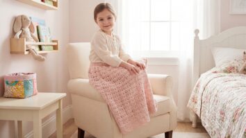 Menina sorrindo com saia de crochê rosa claro em quarto infantil delicado com bichinho de pelúcia e mobiliário claro