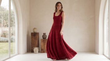 Mulher sorridente usando vestido de crochê artesanal em vermelho intenso em fio de algodão, composição elegante com luz natural realçando textura e caimento sofisticado.
