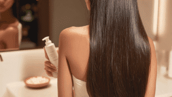 Mulher com cabelos brilhantes e frasco de condicionador em uma das mãos