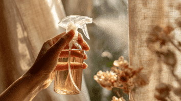 Mão borrifando uma misturinha caseira com spray aromatizador na cortina, uma das dicas para deixar a casa com cheiro de limpeza o dia todo