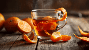 Na imagem temos uma mesa com laranjas, cascas de laraja e uma xicara de chá de cascas de laranja sobre uma mesa