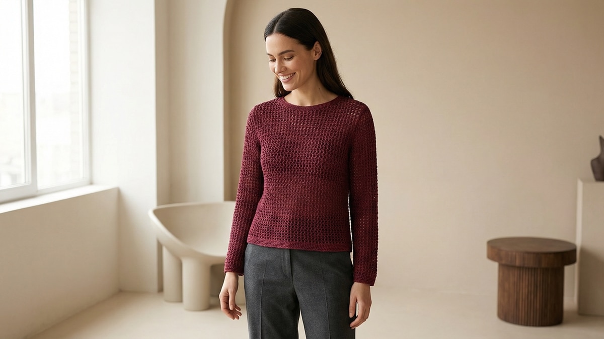 Mulher sorridente com blusa de crochê vinho e calça alfaiataria em estúdio minimalista