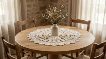 Sala de jantar com mesa de madeira e centro de mesa de crochê off-white com vaso de flores.