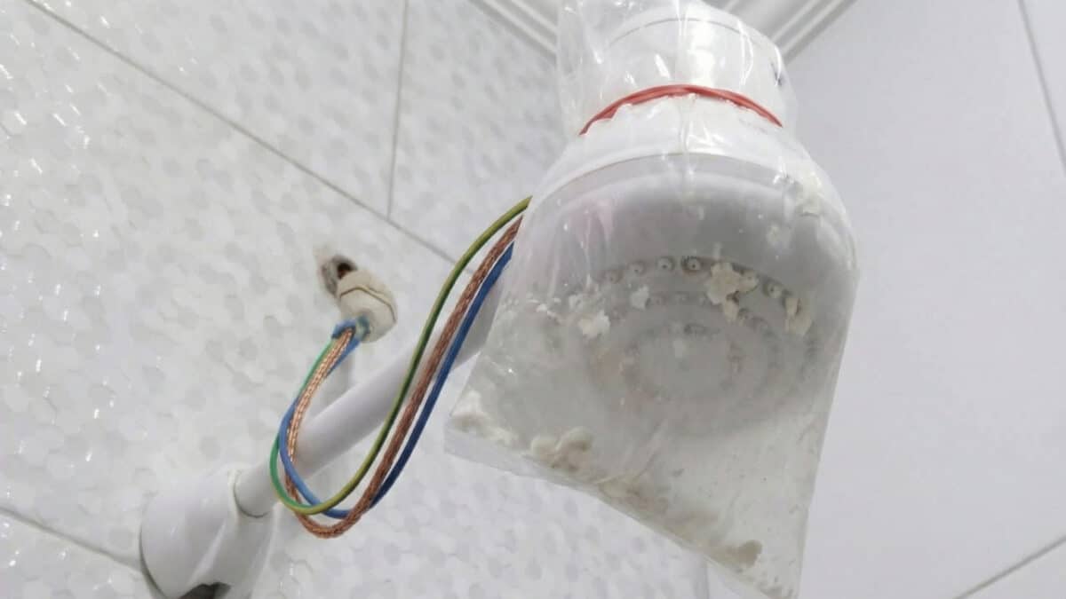 Chuveiro elétrico branco envolto em sacola plástica com resíduos que bloqueavam a pressão da água