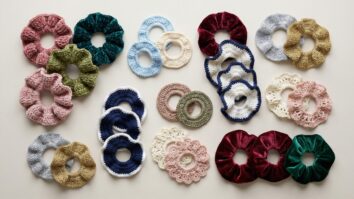 Coleção de scrunchies de crochê em veludo, algodão e lurex organizados sobre mesa neutra.