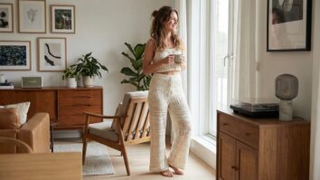 Mulher sorrindo em look completo com conjunto de crochê artesanal: top cropped e calça pantalona em fio de algodão com padrões criativos, em ambiente moderno iluminado.