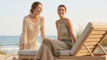 Duas mulheres sorrindo na praia, uma com saída de praia e outra com vestido de crochê elegante.