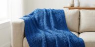 Manta de crochê azul royal com pontos texturizados sobre sofá neutro em sala moderna.