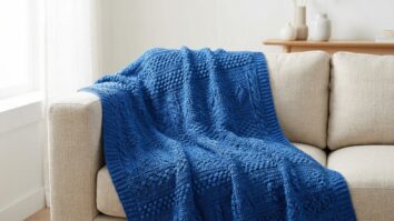 Manta de crochê azul royal com pontos texturizados sobre sofá neutro em sala moderna.