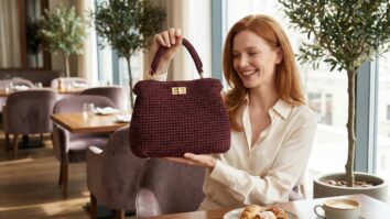 Modelo feminina sorrindo com bolsa de crochê vermelho escuro em restaurante sofisticado