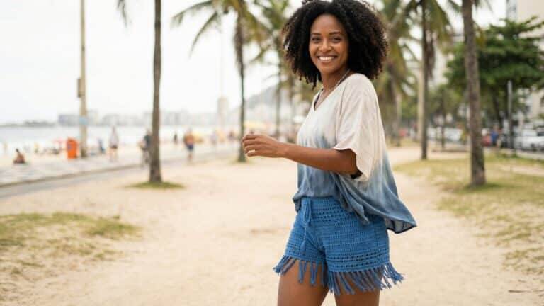 Modelo brasileira sorrindo usando shorts de crochê azul em ambiente de praia, estilo verão boho