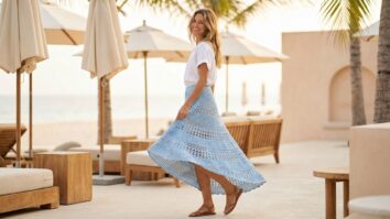 Mulher sorrindo na praia ao entardecer usando saia mullet de crochê azul claro com trama vazada e movimento fluido.