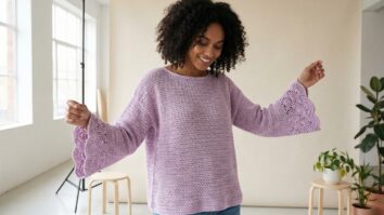 Mulher sorrindo usando blusa de crochê lilás com mangas flare e acabamento em leques