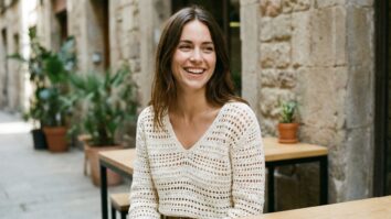 Mulher sorrindo usando blusa de crochê artesanal off-white em ambiente urbano de verão com luz natural