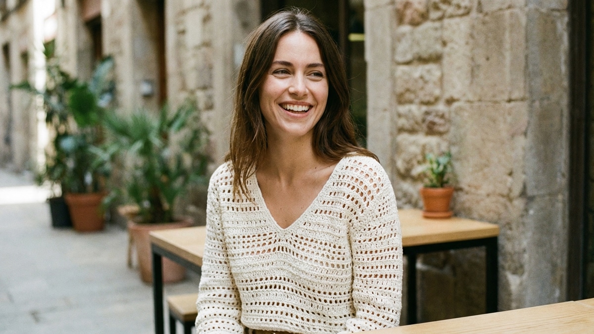 Mulher sorrindo usando blusa de crochê artesanal off-white em ambiente urbano de verão com luz natural