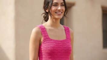 Mulher sorrindo usando blusa regata de crochê em rosa choque com decote quadrado, ambiente de verão