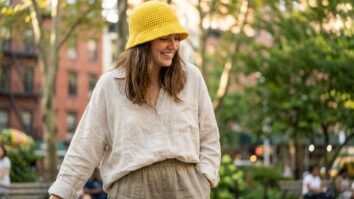 Mulher sorrindo com bucket hat de crochê amarelo em ambiente urbano de verão