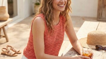 Mulher sorrindo usando regata de crochê coral vibrante com chapéu de palha e óculos de sol