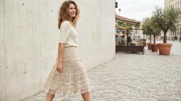 Mulher sorridente usando saia de crochê moderna em tom bege em ambiente urbano com fundo neutro