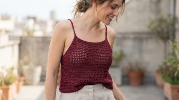 Mulher sorridente em cenário urbano usando regata de crochê vinho de alças finas e trama delicada.