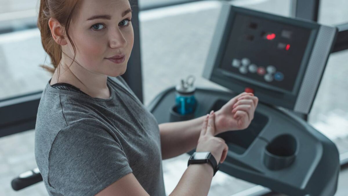 Mulher checando o próprio pulso em esteira na academia