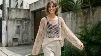 Mulher sorrindo usando blusa de crochê mesh oversized com trama aberta sobre base contrastante em cenário urbano