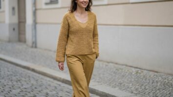 Mulher sorrindo com blusa de crochê mostarda e calça alfaiataria em ambiente urbano