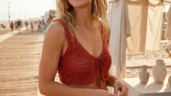 Mulher sorrindo em ambiente de praia urbana, usando cropped de crochê artesanal vermelho com amarração frontal, tecido de algodão com textura bem definida,