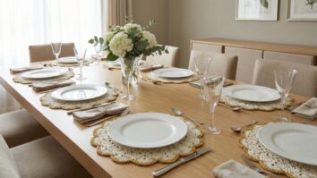 Mesa de jantar com sousplats de crochê branco e detalhes dourados sobre pratos de porcelana em ambiente sofisticado