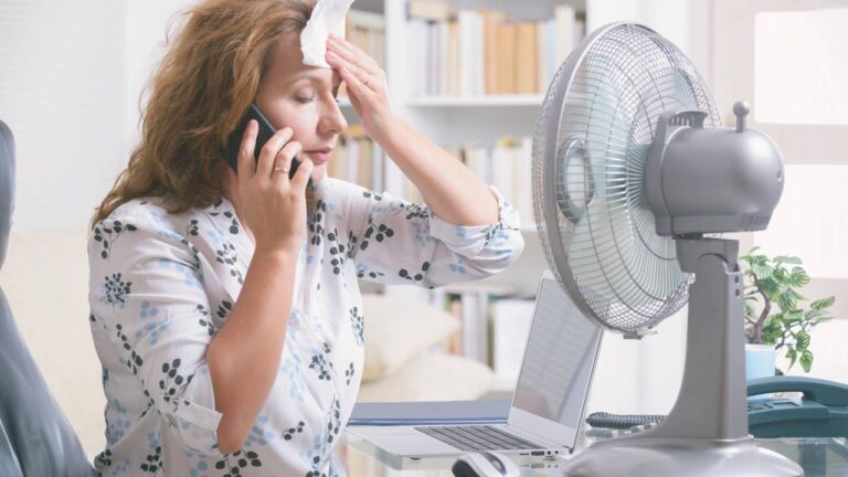 Mulher falando ao telefone em frente ao ventilador em situação de calor extremo