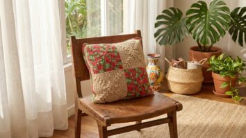 Almofada artesanal de croche cerejeira com blocos em vermelho verde e bege posicionada em ambiente de decoracao brasileira com moveis rusticos plantas tropicais e elementos naturais