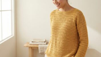 Mulher sorrindo usando blusa artesanal de croche amarela em estudio clean com iluminacao natural suave e estetica editorial minimalista