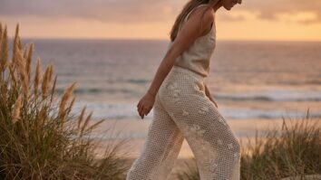 Mulher sorrindo usando calca de croche em ponto rede off-white com bordados florais em ambiente costeiro ao por do sol