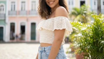 Mulher sorrindo usando cropped ciganinha de croche branco artesanal em cena unica continua em ambiente urbano brasileiro com estetica boho jovem