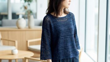 Look feminino sofisticado com blusa de croche artesanal azul marinho em ambiente interno elegante com decoracao neutra e moveis em madeira clara