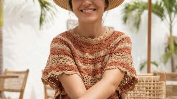 Mulher sorrindo usando blusa de croche artesanal em tom terroso em ambiente de verao brasileiro com iluminacao natural e estetica editorial de moda